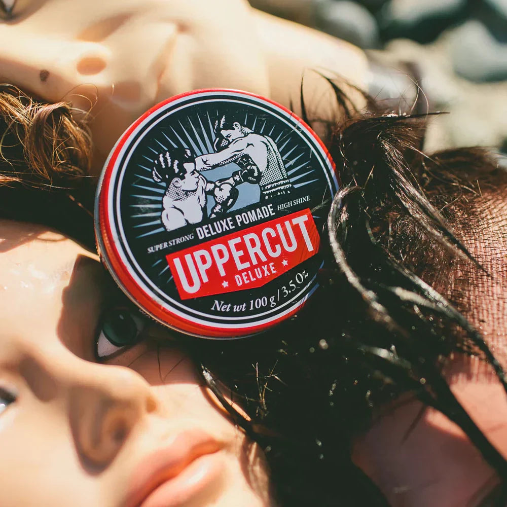 Uppercut Deluxe Pomade resting on top of mannequin heads at the beach