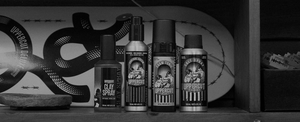 Uppercut Deluxe Clay Spray, Control Cream, Foam Tonic and Salt Spray sitting on a shelf with a skateboard behind them