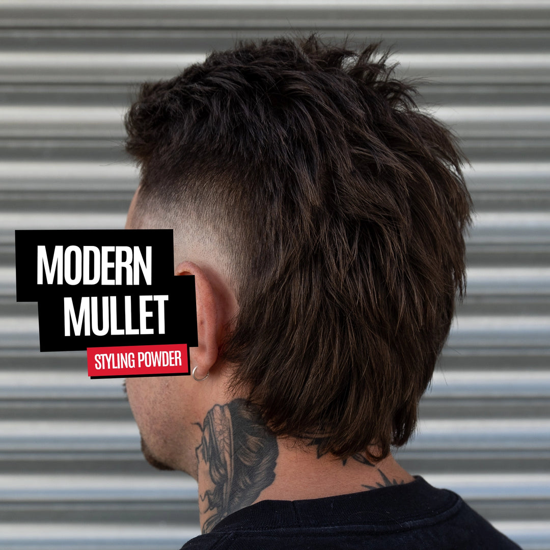 A man shown from the back wearing a dark brown textured pompadour or modern mullet hairstyle with a faded undercut. The background is a corrugated metal wall.