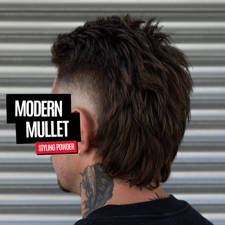A man shown from the back wearing a dark brown textured pompadour or modern mullet hairstyle with a faded undercut. The background is a corrugated metal wall.